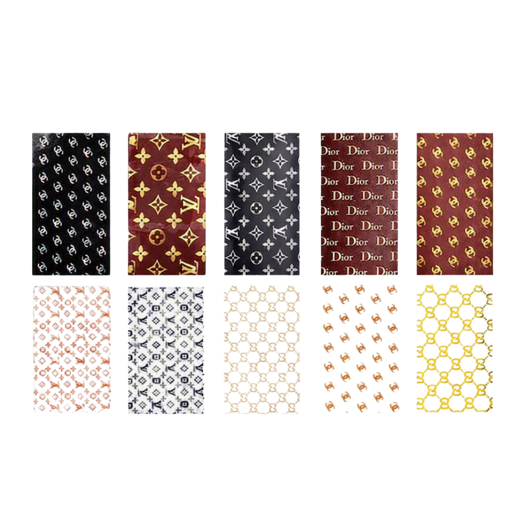 A grid of ten rectangular nail art foil swatches arranged in two rows on a white background. The top row shows black, burgundy, and dark gray monogram-style patterns with repeated Dior text; the bottom row shows lighter monogram-style patterns in peach, navy, cream, tan, and gold.