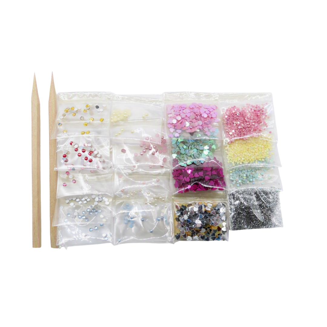 A nail art embellishment set featuring multiple clear plastic bags filled with colorful rhinestones and sequins in pink, green, yellow, silver, and black, alongside two wooden nail sticks on a plain white background.