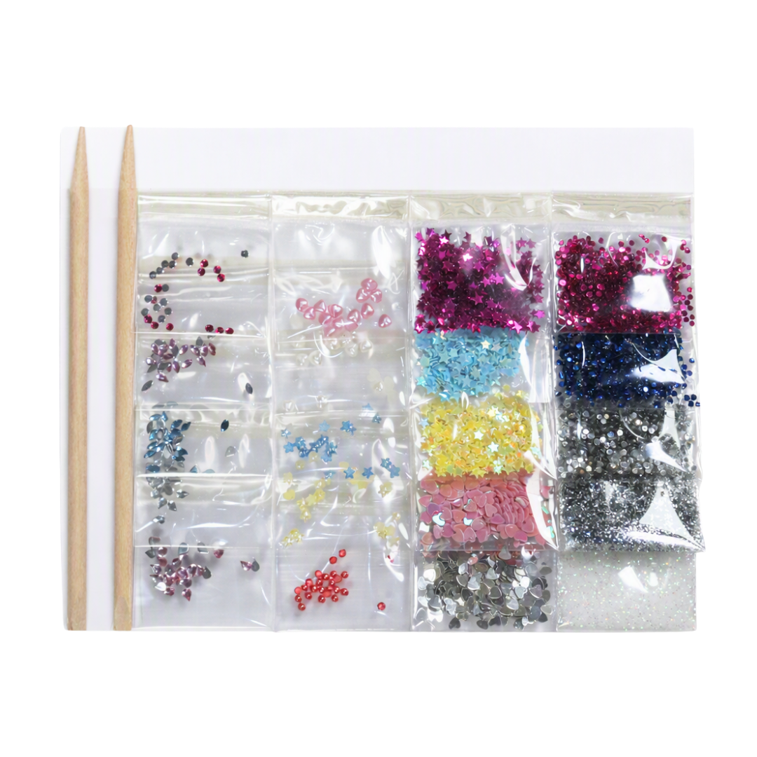 A nail art glitter kit featuring multiple clear plastic compartments filled with colorful rhinestones, sequins, and glitter in pink, blue, yellow, silver, and black, alongside two wooden nail sticks on a white background.