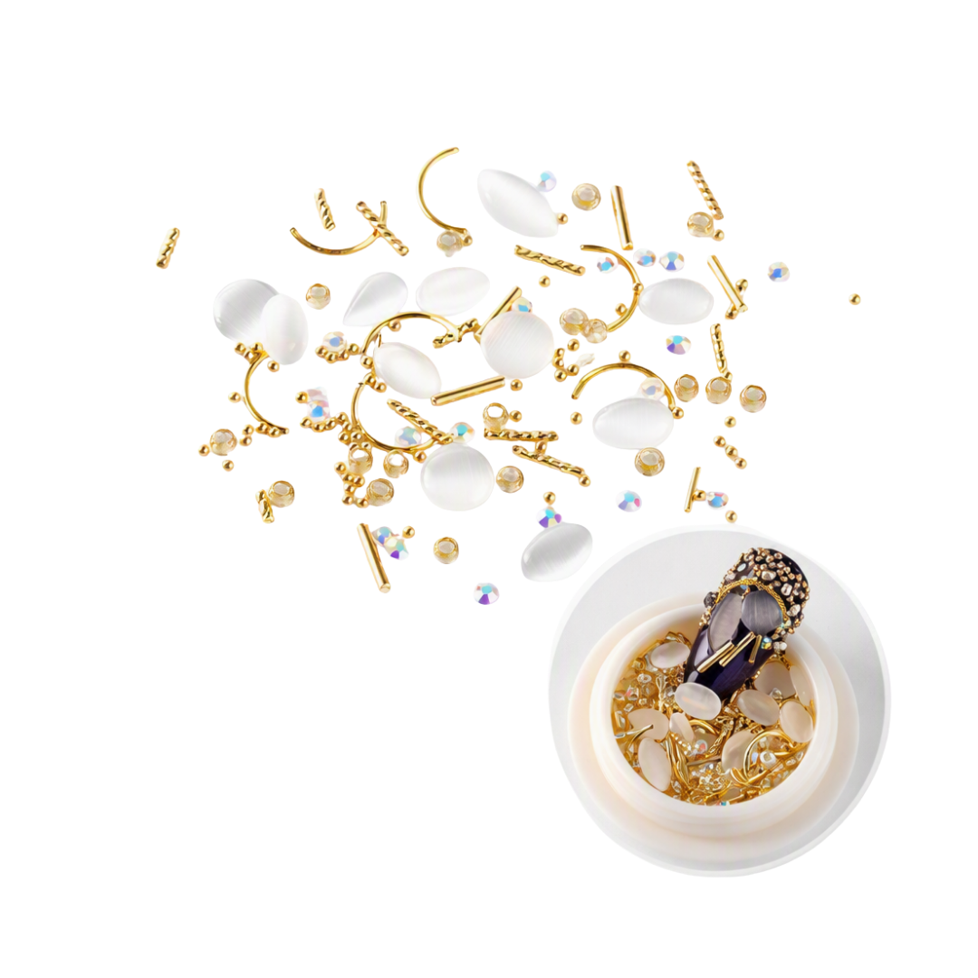 Gold and white nail art embellishments, including rhinestones, beads, and curved wire, scattered on a white background with a small white dish containing a decorated nail sample.