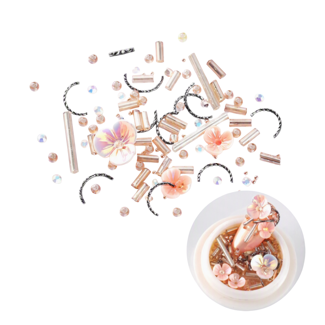 Rose gold and pink 3D Nail Art embellishments scattered on a white background, including metallic tubes, iridescent beads, floral pieces, and a small inset showing them arranged in a decorative bowl.