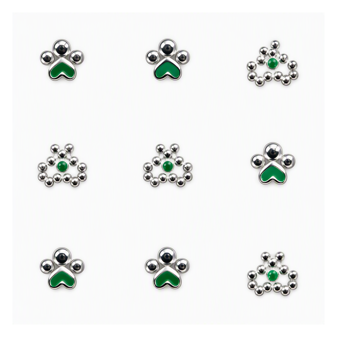 Nine small silver-toned nail art designs arranged in a 3x3 grid on a white background. Each earring features a green enamel accent in a paw-print or floral-like shape, with some pieces including a small central green stone.