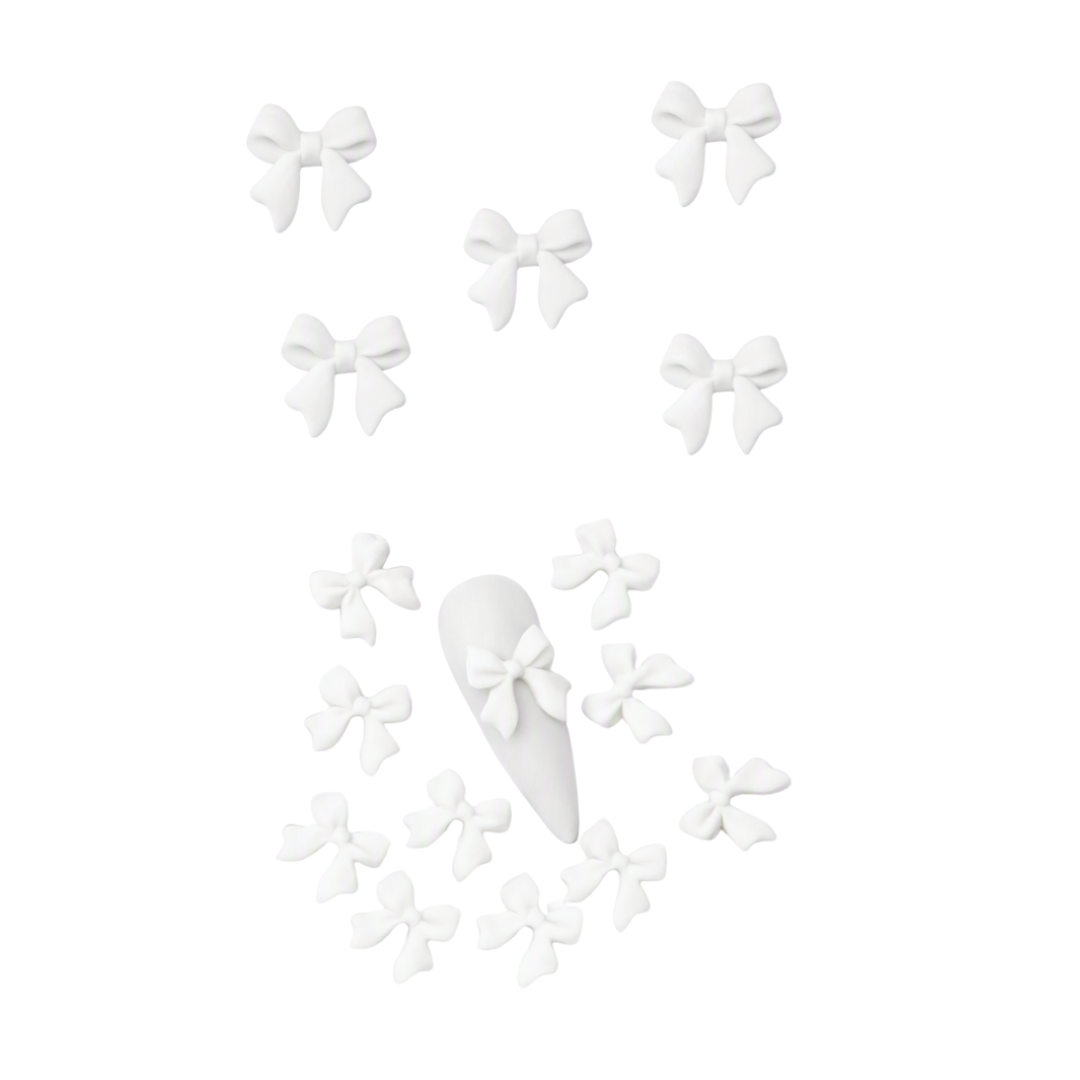 White nail art embellishments multiple small bows and a pointed nail tip shown on a plain white background