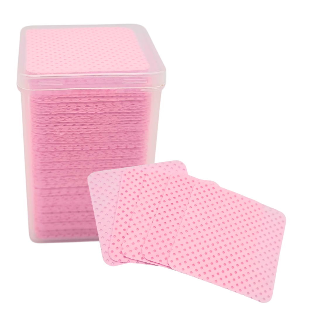 Pink textured square lint free pads stacked inside a clear plastic container with three pads fanned out in front on a white background.