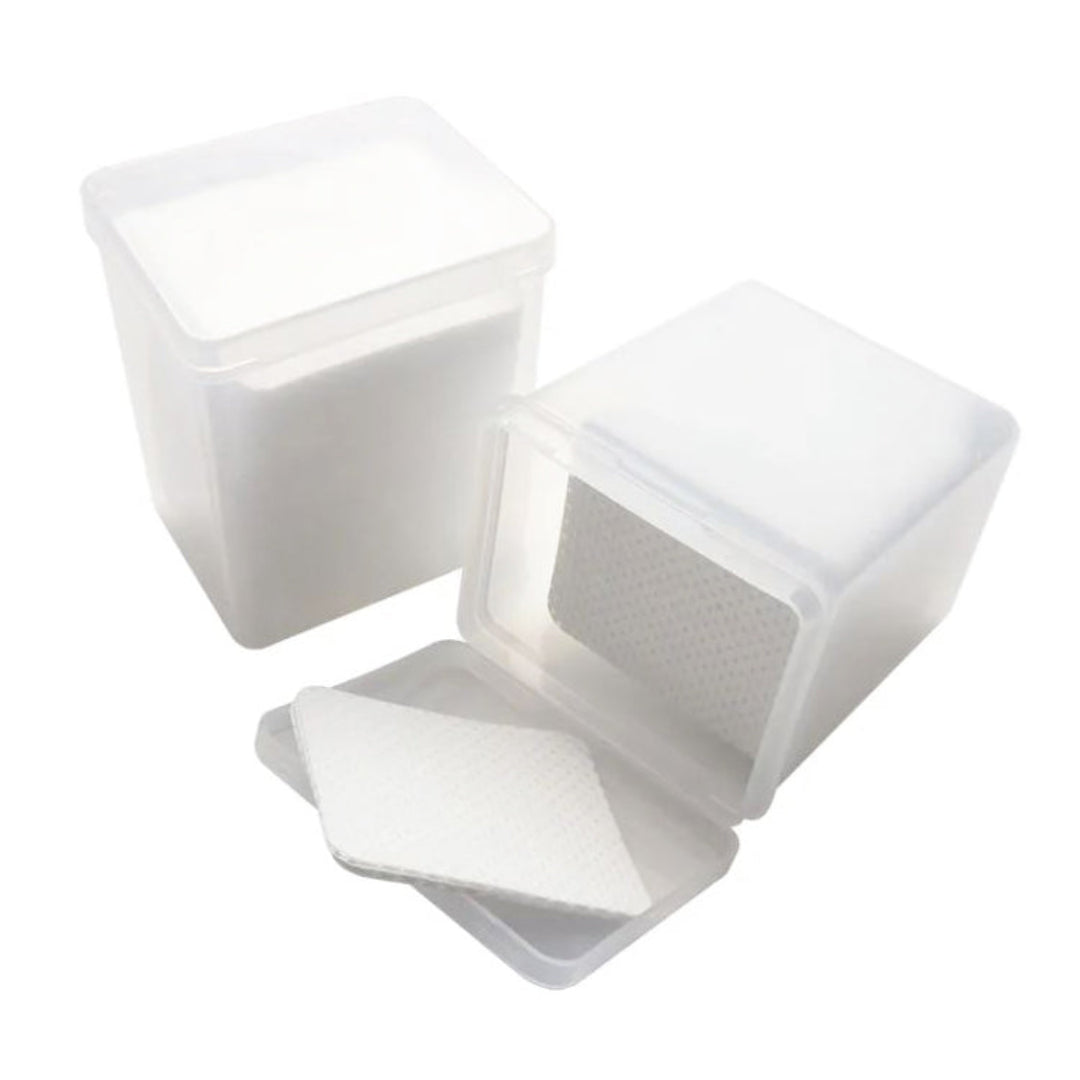 White textured square lint free pads stacked inside a clear plastic container on a white background.