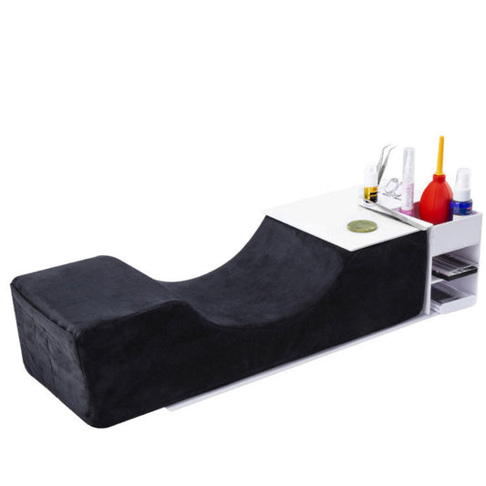 A salon lash extension console with a black plush cushioned headrest and a white side organizer holding lash tools and styling products, shown on a plain white background.