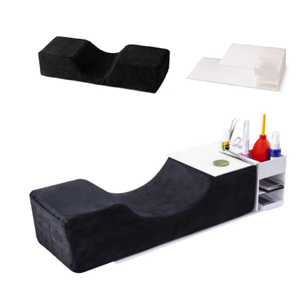 A salon lash extension console with a black plush cushioned headrest and a white side organizer holding lash tools and styling products, shown on a plain white background.