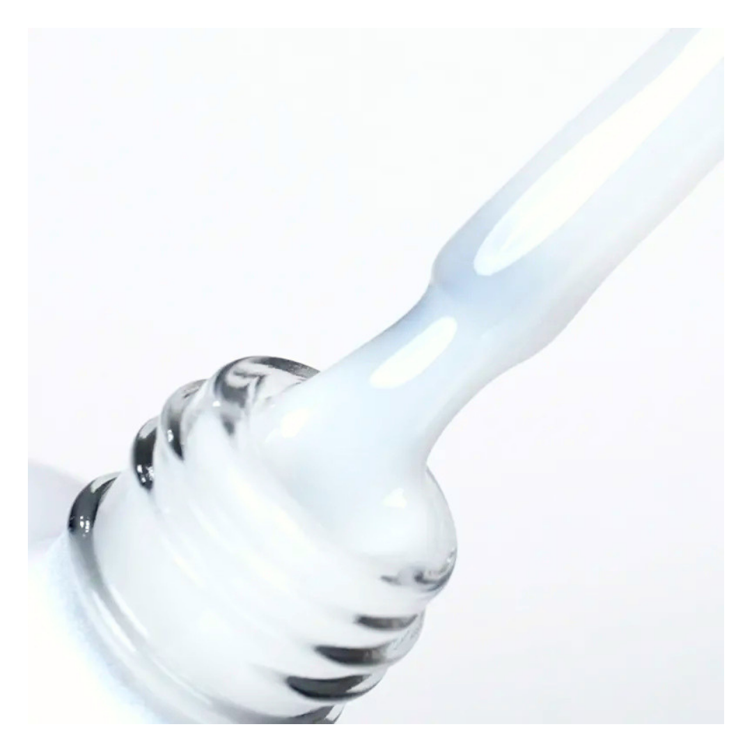 A close-up of a gel nail brush dipping into bottle containing a milky white Leo Laque topcoat, against a clean white background.