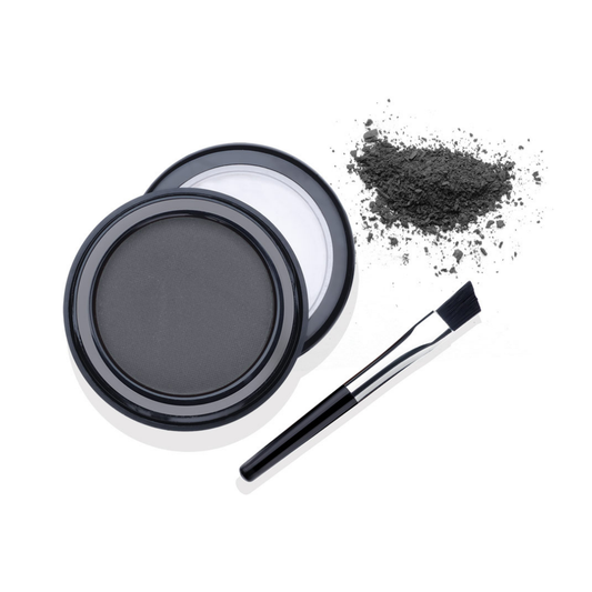 A black cosmetic eyebrow powder compact shown open with a small, angled brush and a small pile of loose powder on a white background.