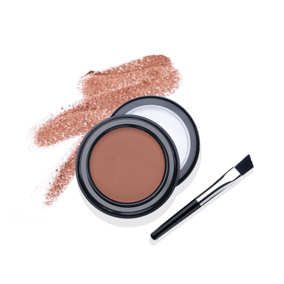 A round makeup compact with a pressed eyebrow powder in a warm medium brown shade, shown open with a black lid and a small, angled brush beside it. A matching textured powder swatch is smeared behind the compact on a clean white background.
