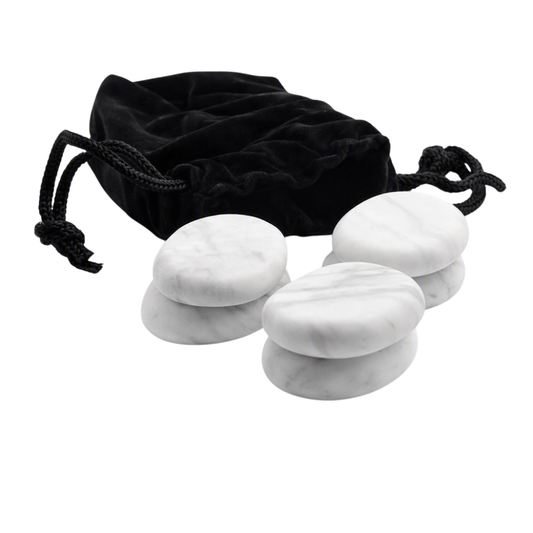 Six white marble massage stones arranged in front of a black velvet drawstring pouch on a plain white background.