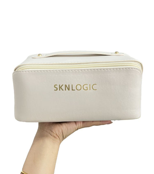 Beige cosmetic bag with 'SKNLOGIC' branding held by a hand on a white background