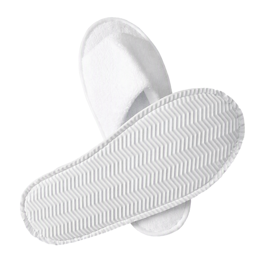 A pair of white slippers shown on a plain white background, with one slipper placed on top of the other to display both the soft textured upper and the patterned sole.
