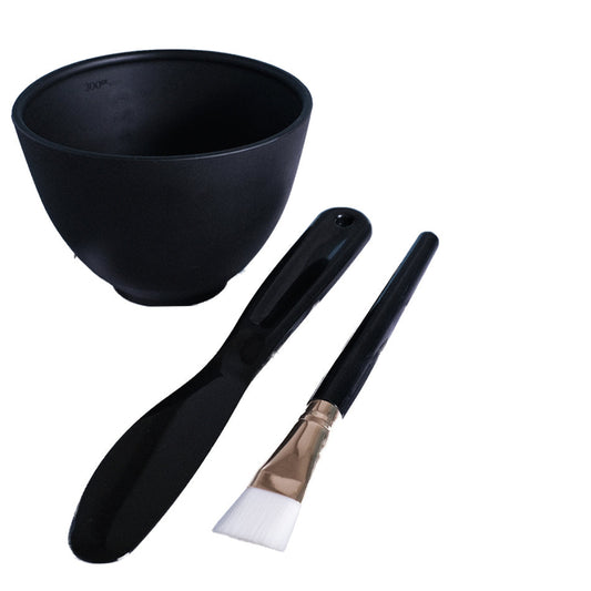 Black flexible rubber mask bowl, spatula, and small clear containers on a white background
