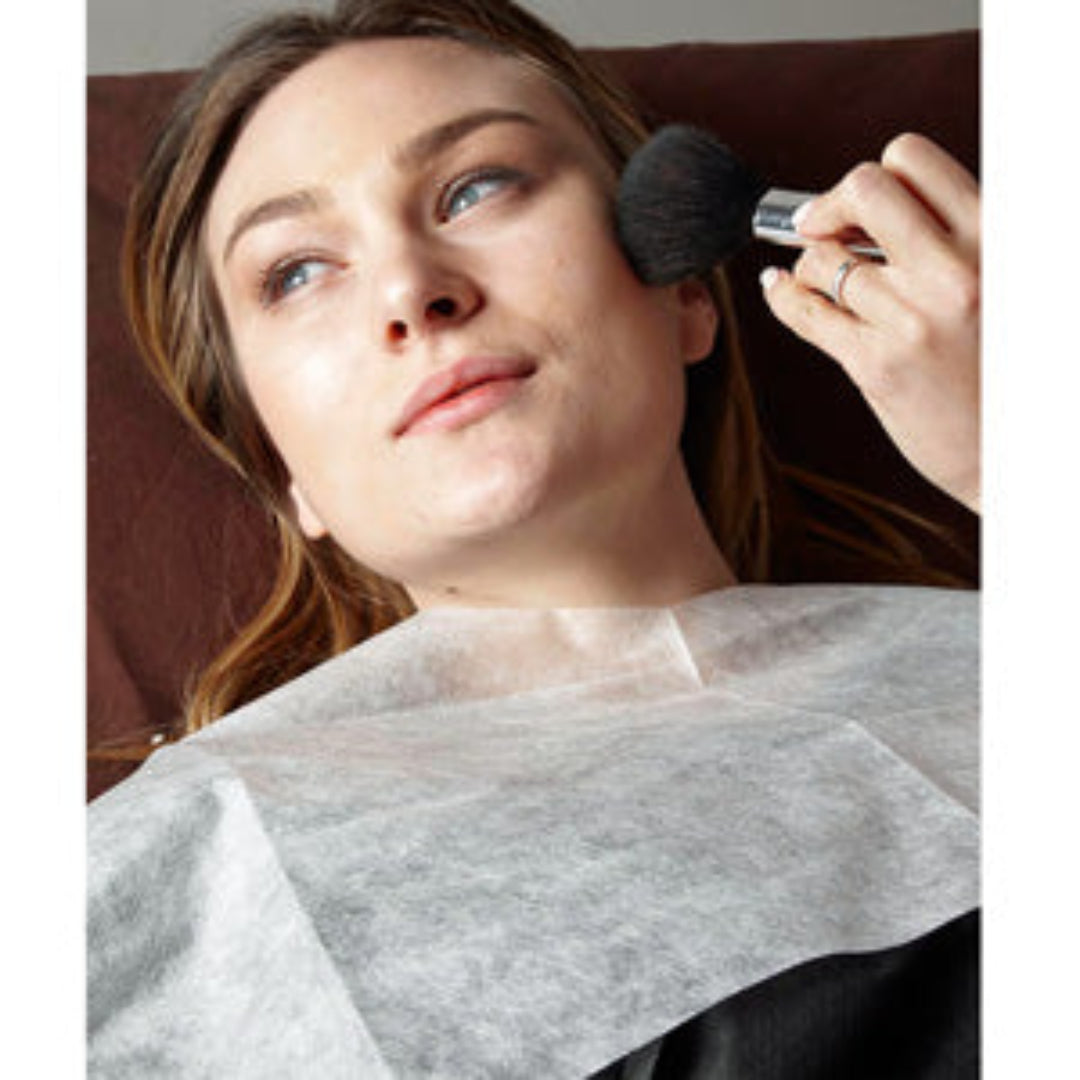 Z703A Disposable Makeup Bib with Ties | Woman with a white non-woven makeup bib and a hand applying powder to the face