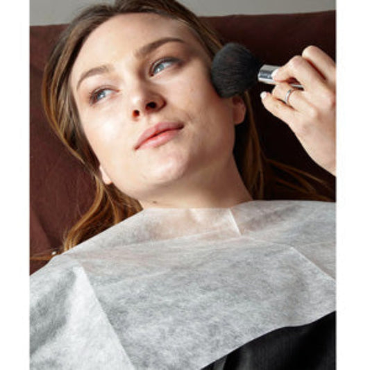 Z703A Disposable Makeup Bib with Ties | Woman with a white non-woven makeup bib and a hand applying powder to the face