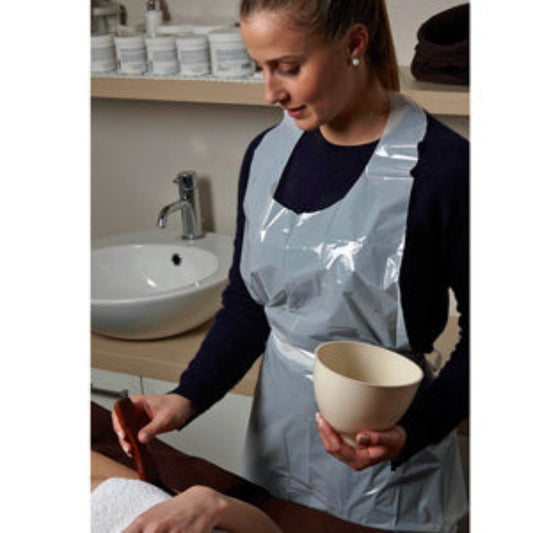 Z704A Plastic Disposable Therapist Apron 100piece | A woman wearing navy clothing with a white plastic covering front of her body while apply products to a persons body